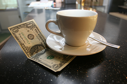 coffee cup resting on top of a dollar bill on a table