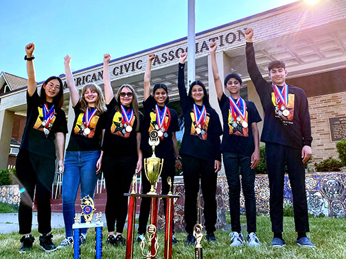 Proud members of the American Civic Association's Odyssey of the Mind team stand in front of the American Civic Association building with their trophies and medals. 
