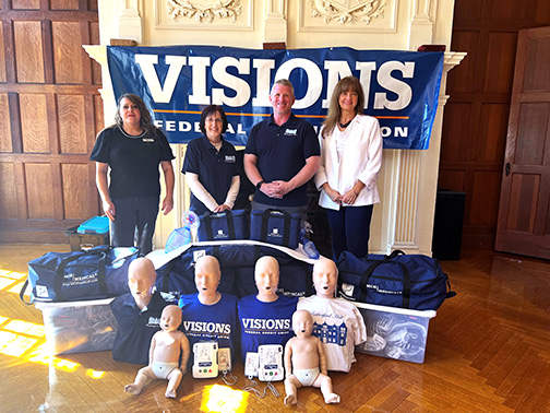 Visions NJ Community Development Liaison, Shari, smiles with a few members of the Allamuchy Township Board of Education behind first aid supplies, AED training packets, and several professional CPR manikins that are dressed in Visions shirts.