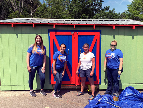 Visions employees stand in front of a freshly painted shed with a volunteer coordinator at the Discovery Center in Binghamton, NY.