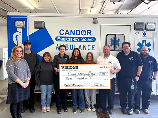 Pictured are members of the Junior Member Healthcare Initiative, Abbey (Community Development Specialist of Tioga County), Curtis (Operations Chief - Candor EMS), and members of the Candor EMS squad standing in front of an ambulance holding a check