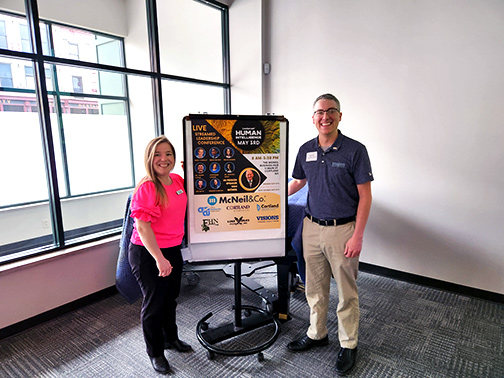 Visions employees Sarah (left) and Mark (right) are pictured next to the LeaderCast sign, which contains information about the day's events.
