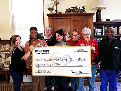 Visions Community Development Liaison, Sarah, poses with members of the Cortland Community Group ESL as she presents them with a jumbo check for a grant to purchase supplies for their students.