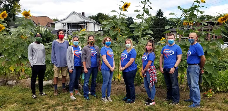 Visions employees Kali, Cassandra, Clairissa, Lindsay, Samantha, Devin, and Anastasios smile with farm managers of VINES. They are standing in front of a family of sunflowers in the VINES beautiful outdoor gardens in downtown Binghamton, NY.