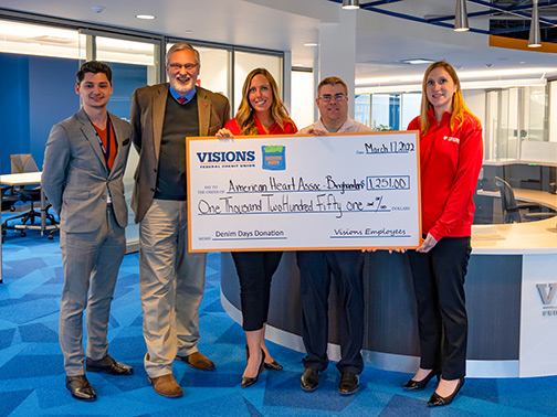 Visions employees Ciano, Kali, and Dan smile while presenting a jumbo Denim Days check to American Heart Association representatives in the Visions Headquarters Lobby in Endicott, NY.
