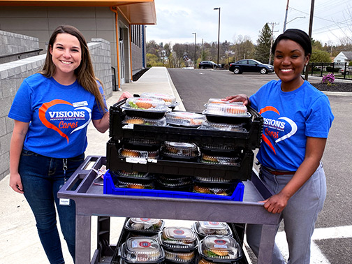 Employees of our Community Development department, Samantha and Aisha, smile for a quick photo with a full cartload of hot and freshly made meals to be brought to our local healthcare professionals at UHS Hospital in Binghamton, NY. 
