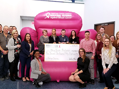 Visions FCU staff sitting in a giant pink chair presenting a $7,500 sponsorship check to Making Strides Against Breast Cancer of Broome County