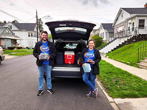 Visions employees Peter (left) and Jessie (right) pictured getting meals out of the back of a vehicle for delivery.