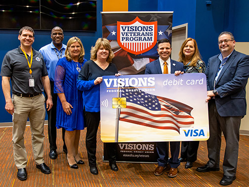 Visions FCU leadership holding an enlarged version of the Visions Americana debit card design with staff from Operation Homefront