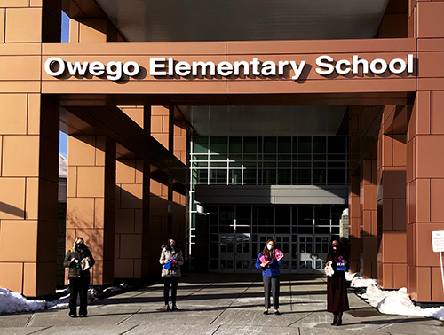 Standing outside Owego Elementary School, Visions FCU employees hold up winter items donated by our Owego and Apalachin offices.