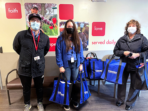 Visions Marketing Clerk, Emily, poses with Rescue Mission staff in Syracuse, NY as she delivers donated items in branded totes.