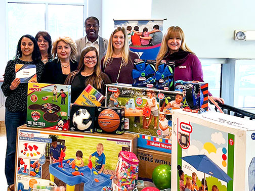At the grand opening of our Ridgewood, NJ office, Visions staff smile and pose near a table of donated items with representatives and the CEO of the local YMCA.