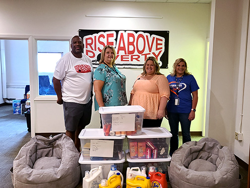 Pictured is Visions staff and Reggie from Rise Above Poverty standing behind a pile of donated personal care items