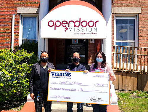 Visions employee, Regina Seabrook, is pictured holding a large check in front of Open Door Mission in Rochester, NY with two of their representatives.
