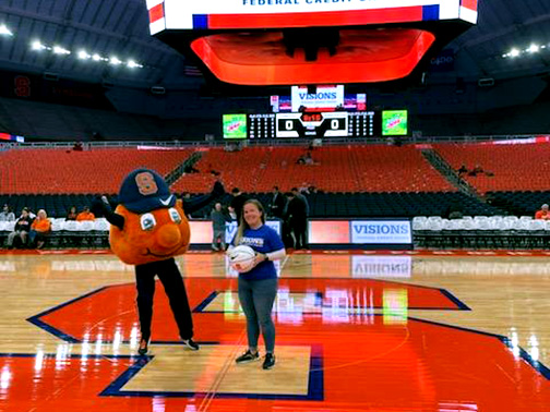 Visions Community Development Liaison, Sarah, smiles on the SU Basketball court with a basketball and their mascot, Otto the Orange.