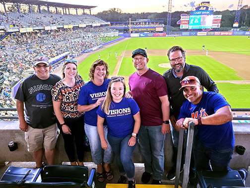 Some of our Syracuse employees and their guests smile from the balcony of the Visions suite at the Syracuse Mets baseball game.