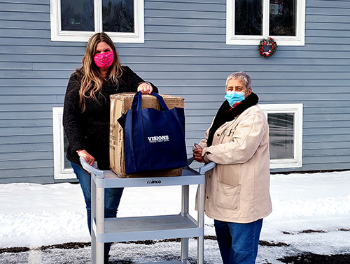 A Visions FCU employee stands with a box of 100 Visions branded tote bags presented to a representative of the North Syracuse Christian Church Food Pantry as a donation.