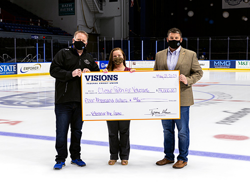 Visions employee, Sarah Parton, presents a giant check on the ice to representatives from the AHL Hockey team, Syracuse Crunch, and charitable organization Clear Path for Veterans.