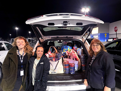 Standing beside an open trunk filled with several tote bags of holiday food items are some of our Watkins Glen branch staff.