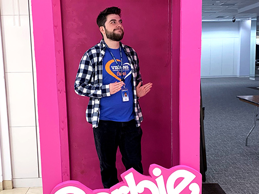 Visions employee, Peter, posing in a pink Barbie box with stiff, Barbie-style hands. 