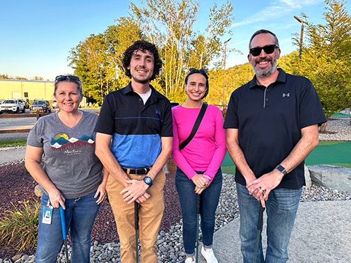 Four smiling Visions employees posing on the mini golf course on a sunny evening.