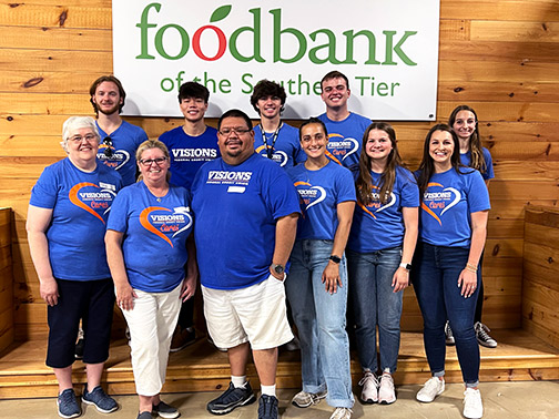 Visions employees and interns standing in front of a white banner with the Food Bank of the Southern Tier logo.
