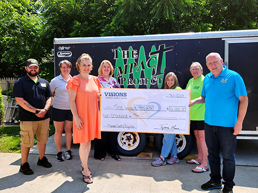 Representatives of the Impact Project and Visions employees pictured with a large check in front of the Impact Project construction trailer.
