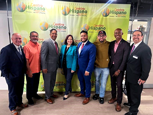 Visions employees and representatives from Centro Hispano posing in front of a green and yellow backdrop with the text: Centro Hispano Hispanic Center and El Centro…the HEART of Reading. 