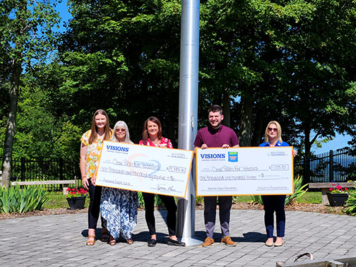 Two representatives from Clear Path for Veterans and three Visions Employees posing with two large checks on a sunny August morning.