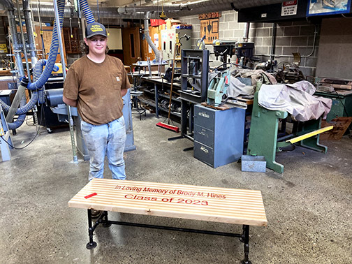 Newark Valley graduate, Laine, pictured in a shop with the wooden and steel bench built in memory of classmate Brody Hines.