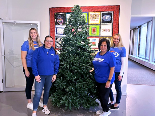 Visions employees Christi, Megan, Alexa, and Laura pictured next to a Christmas tree. 