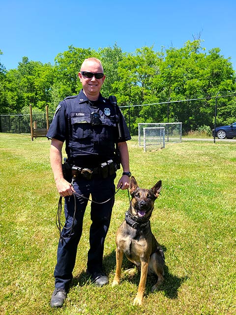 A Rochester Police Officer stands with his K-9 partner, Brock.