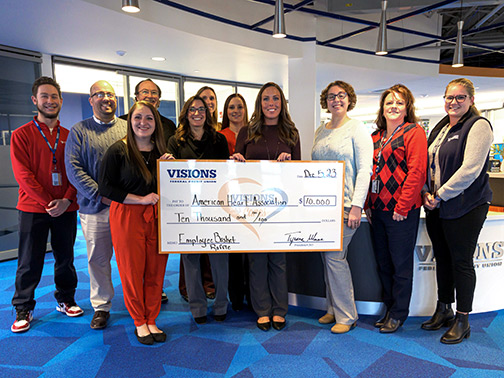 Visions employees posing with American Heart Association representatives and a large check in an open lobby area.