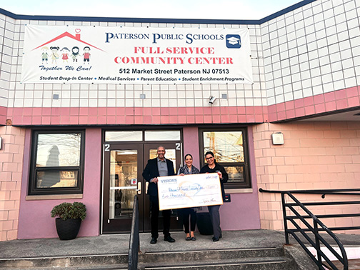 Two representatives from the Paterson Public Schools Full-Service Community Center and Visions employee, Tatiana, holding a check. The three smiling representatives are standing in front of the Community Center.