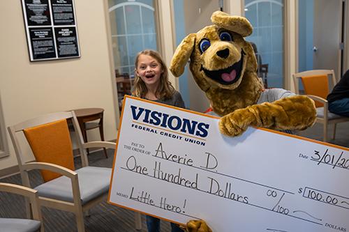 An excited Averie smiles with Kirby Kangaroo as they hold a giant check for $100.