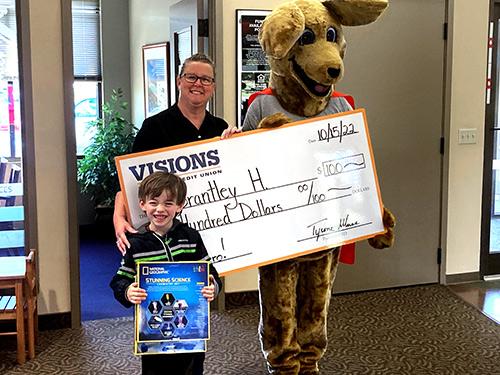 Brantley standing with Kirby the Kangaroo holding a $100 giant check and hit science kits!