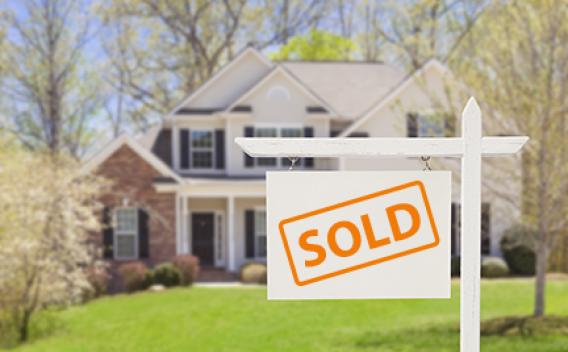 A sign with the text "SOLD" is standing in the front yard of a house.