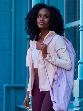 Woman looking upward, walking out of a building with watch and backpack.